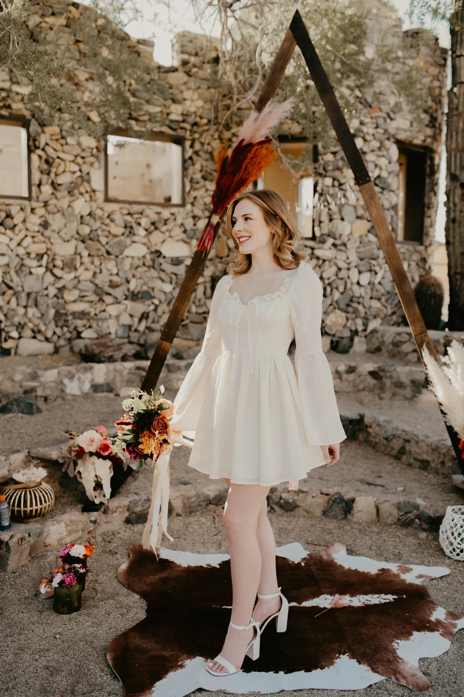 The bride smiles beneath the wooden ceremony arch, dried grasses and ribbon hung overhead.