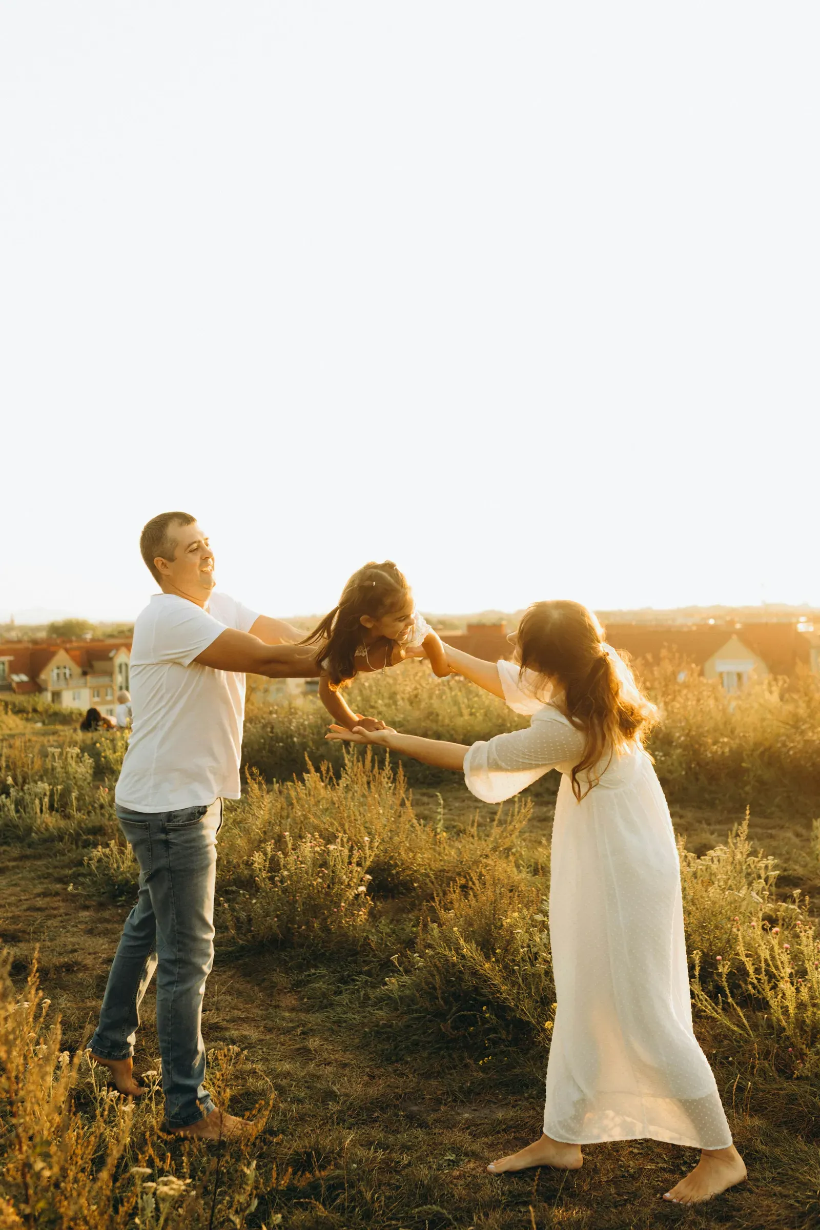 Mom and Dad swing their girl between them on the dirt track through the meadow.