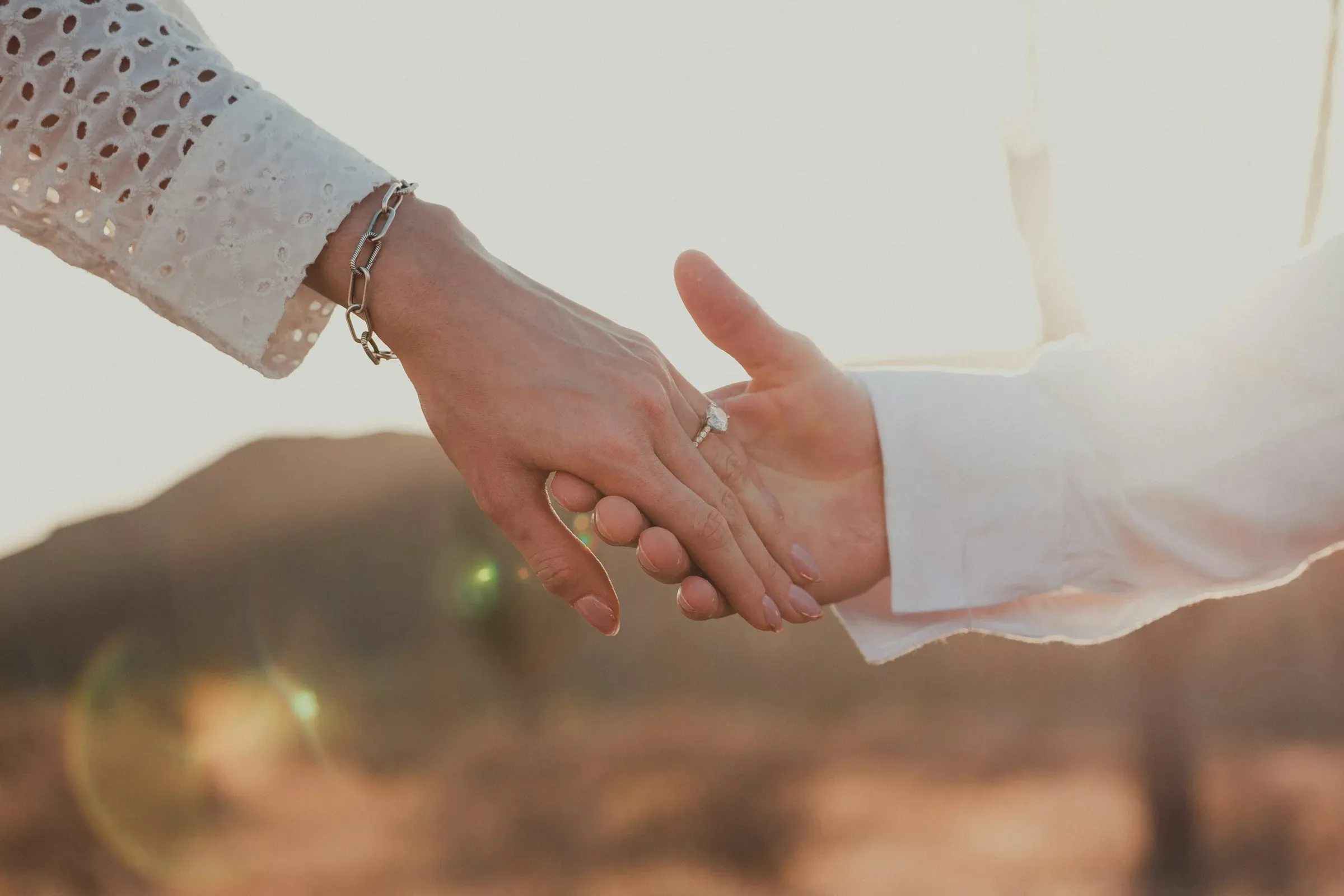 A close frame of their hands at last light, her new ring catching the sun.