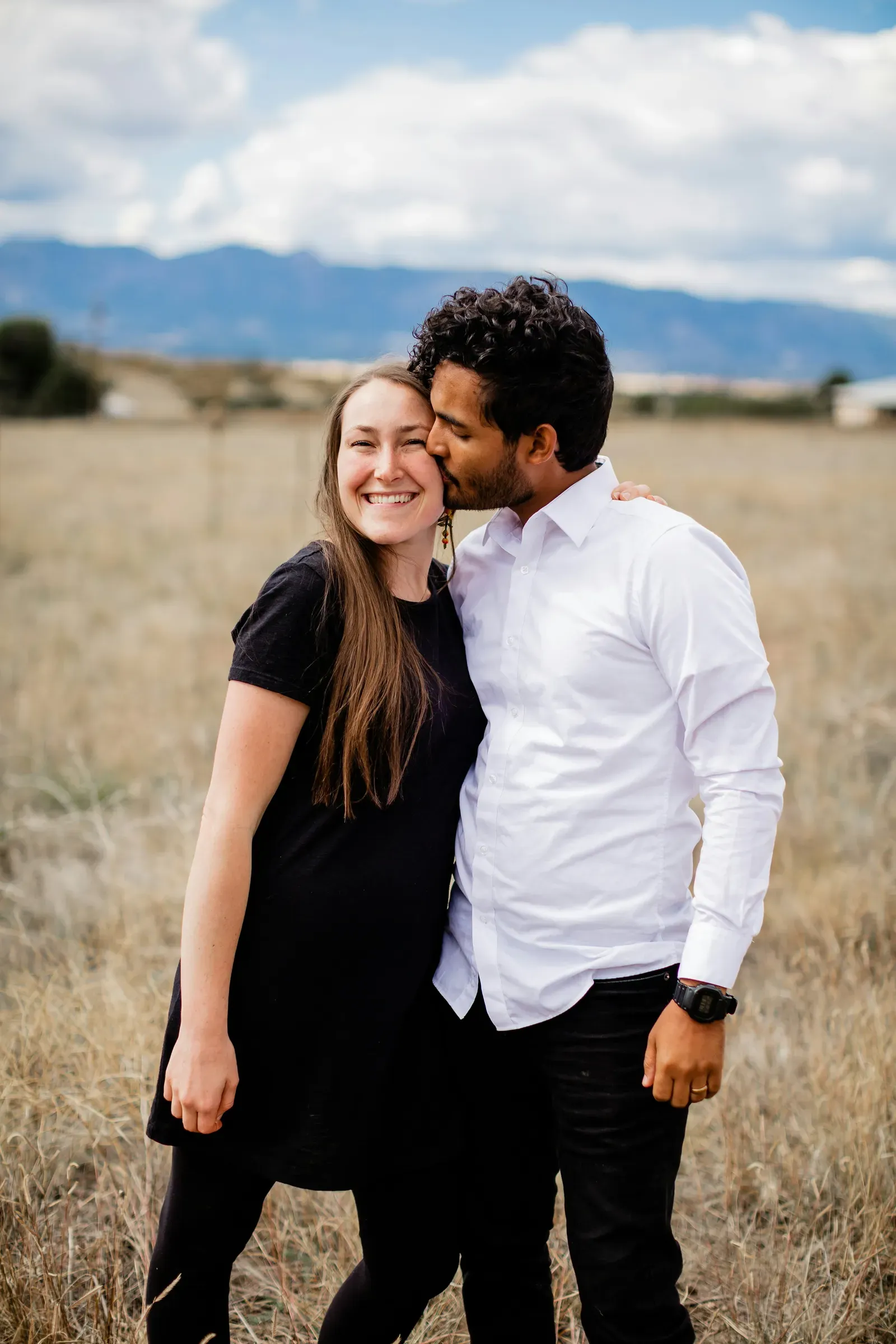A kiss on the cheek in the June-cured grass, the ridge hazy blue behind them.