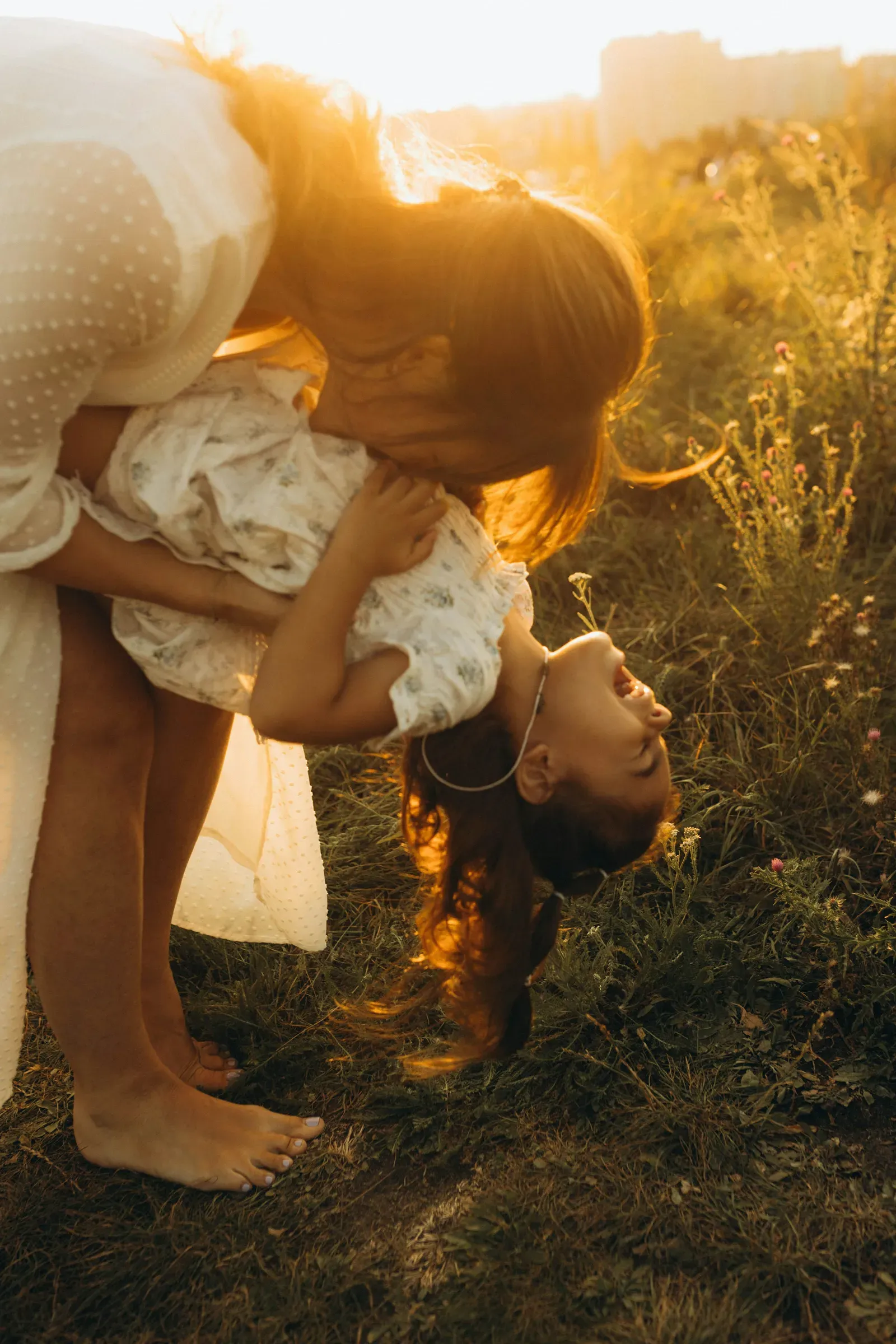 Mom flips her upside down in the tall August grass, both of them mid-laugh.