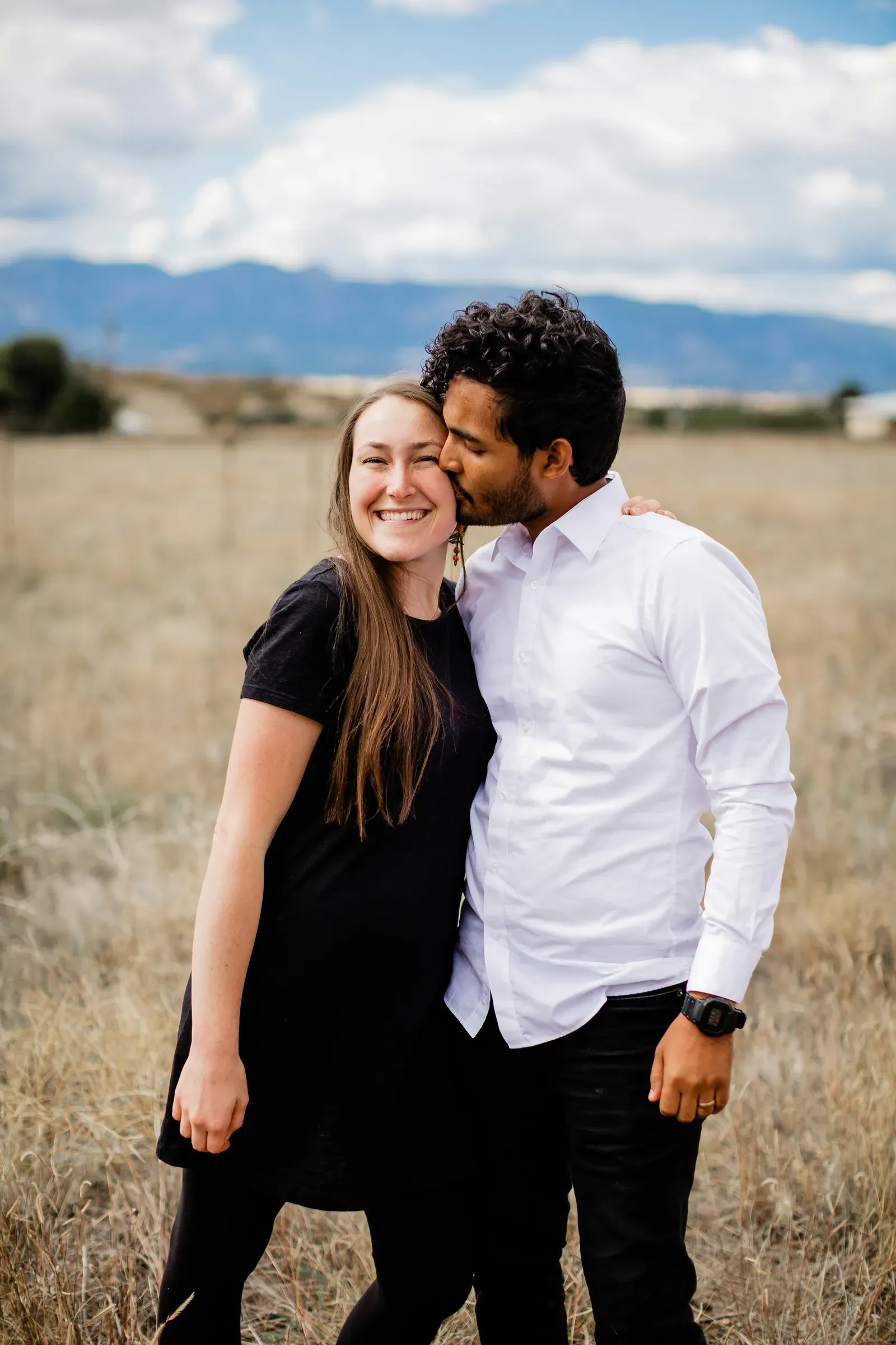 He kisses her cheek while she smiles straight at the camera.