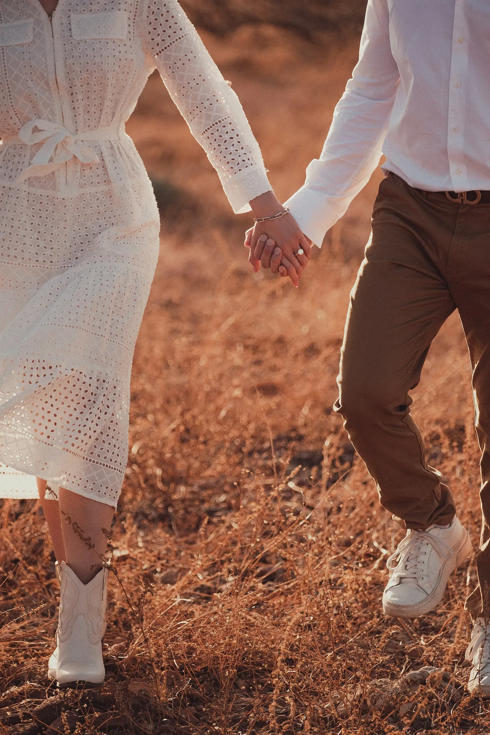 Their hands linked as they walk through the dry grass, boots dusty from the trail in.