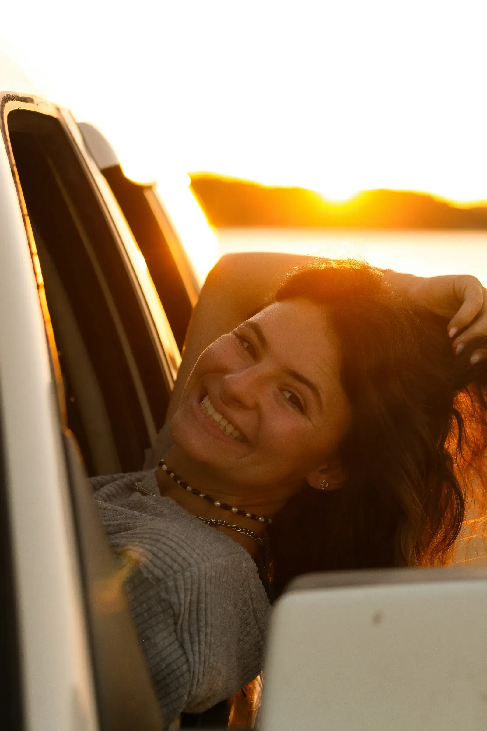 Sun flare off the lake as she leans back in the window, hand in her hair.
