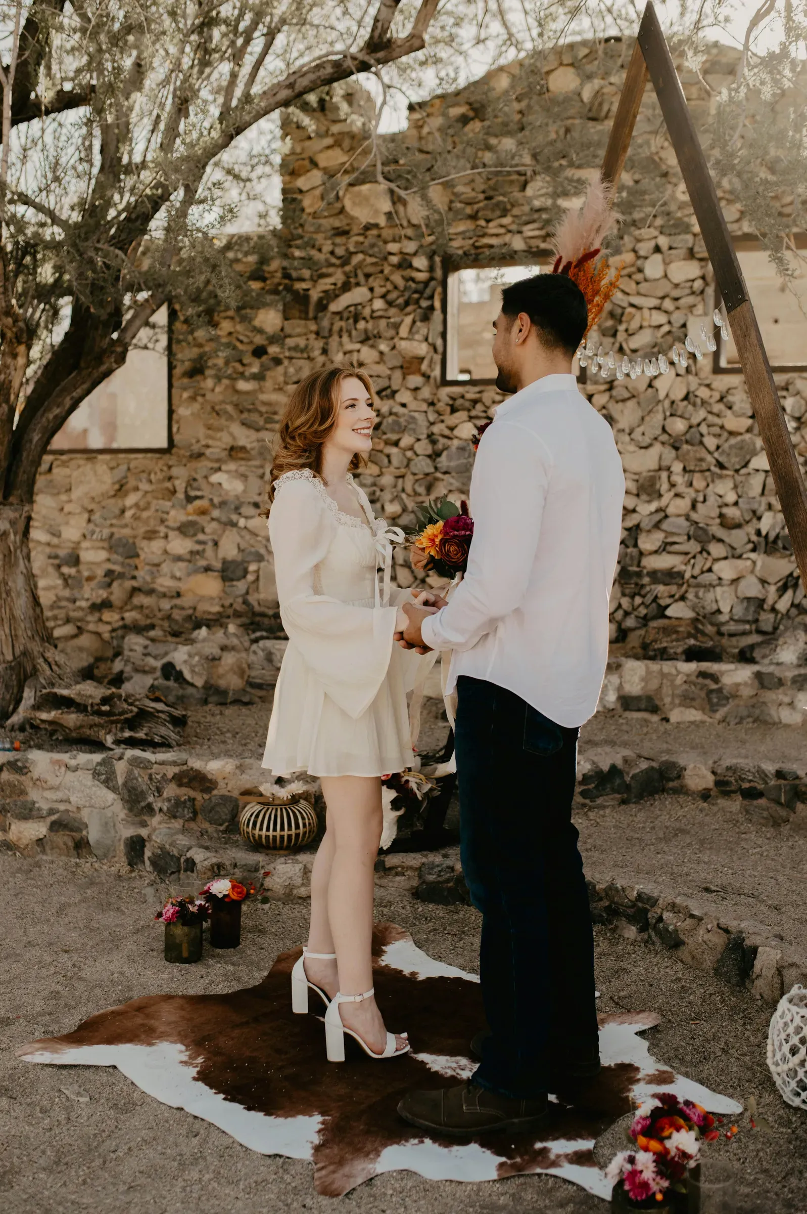 The couple faces each other for their vows under the arch at the old stone homestead.