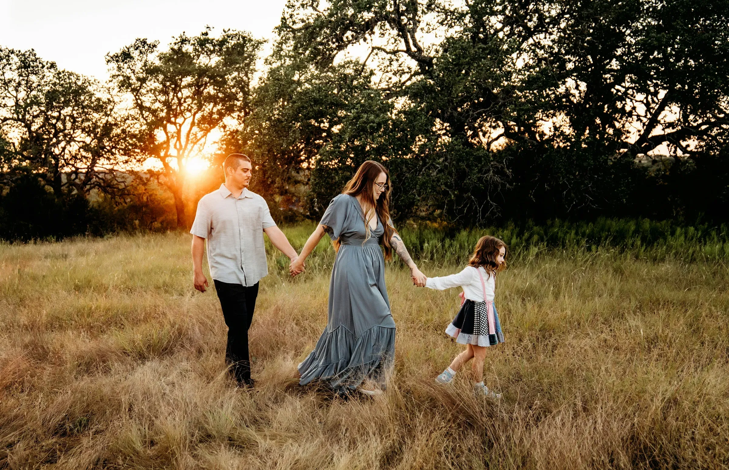 All three walking hand in hand through the tall grass, golden light on their backs.