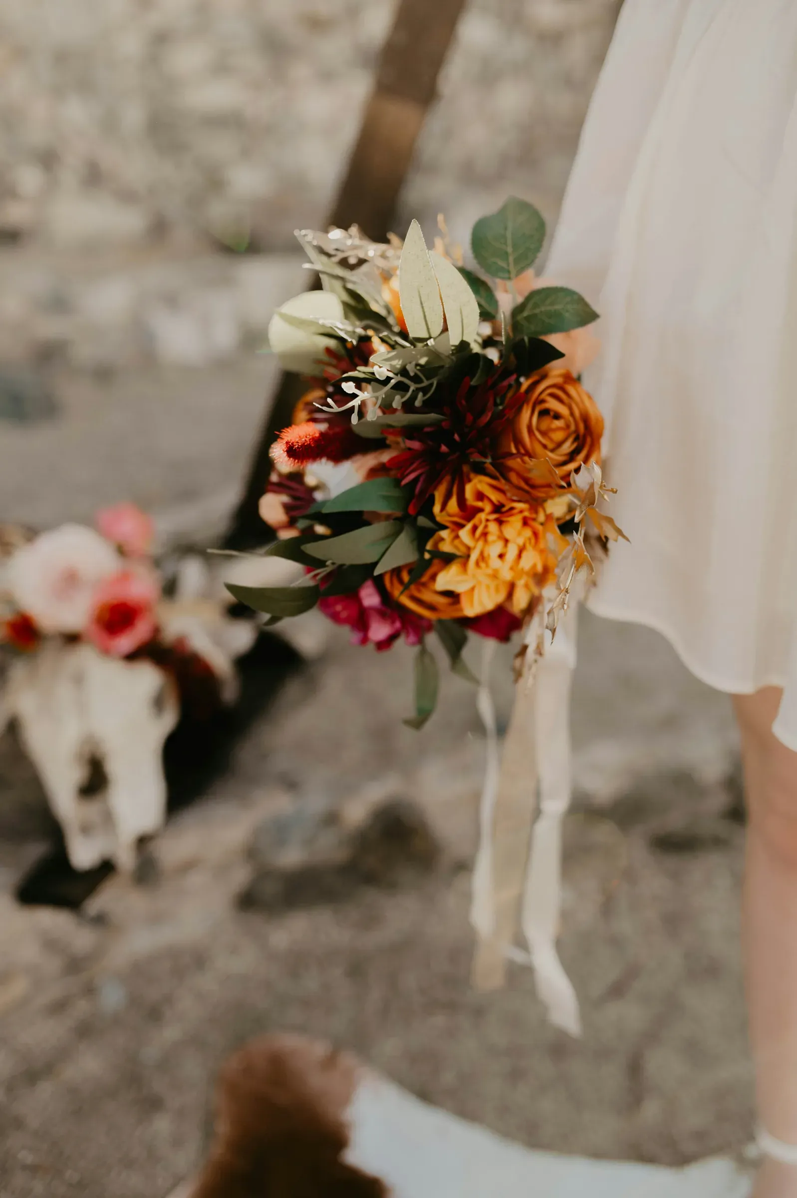 A detail of the bouquet hanging at the bride's side, sand and ceremony flowers at her feet.