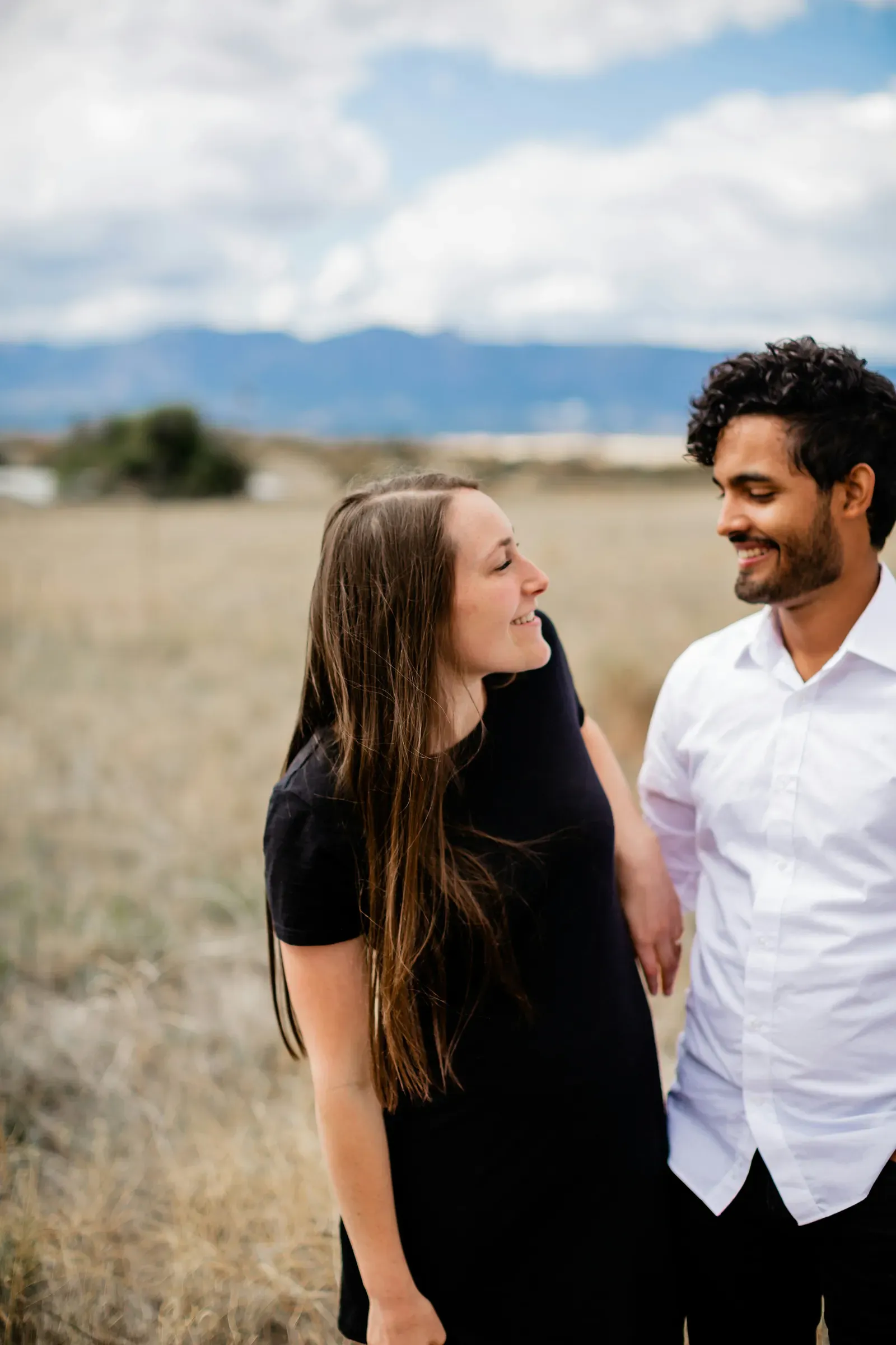 She looks up at him from a low angle, field and sky behind.