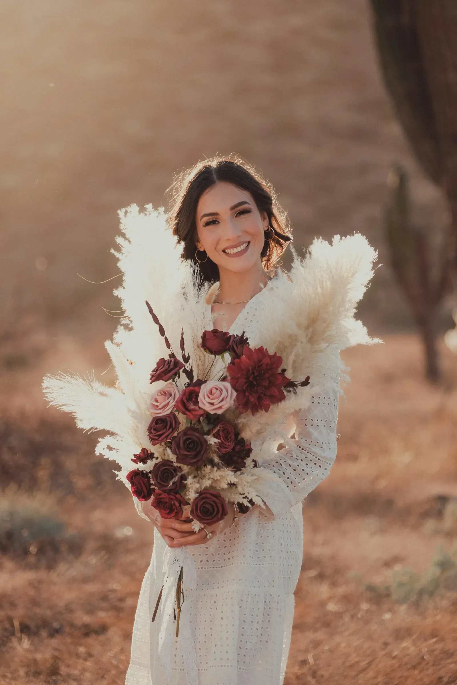 The bride grins over her armful of pampas and dark roses in the last of the light.