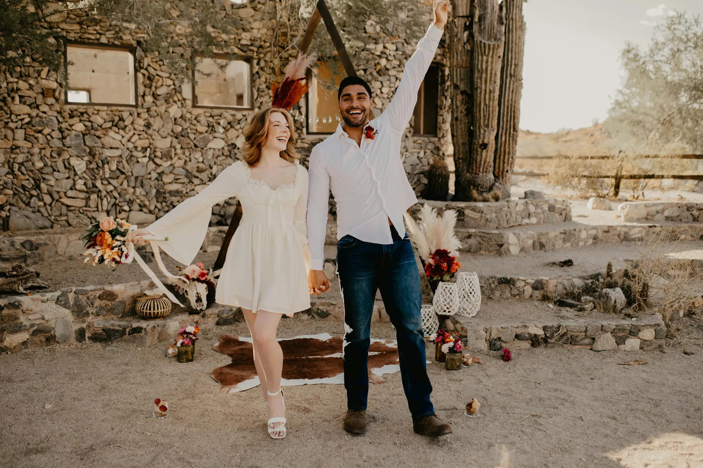 The groom throws an arm up in celebration as the two of them stand hand in hand on the cowhide rug.